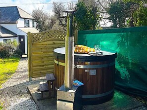 Een hottub met een houten terras en schoorsteen, omgeven door een houten hek en een groene wand.
