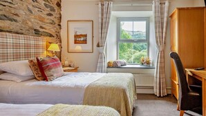 Ein Schlafzimmer mit zwei Betten, einem Schreibtisch, einem Stuhl, einem Fenster mit Vorhängen, einer Lampe und einem gerahmten Bild an der Wand.