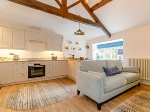 A modern kitchen with white cabinets, a built-in oven, and a dining area with a grey sofa and a 'Welcome' pillow. - 1 Bed in Hope Valley (oc-89720) (Hope)