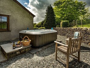 Ein Whirlpool mit Steinwand und Holzstuhl vor einem Haus.