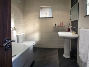 Een badkamer met een bad, toilet, wastafel en een raam met zonwering.