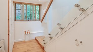 A modern staircase with glass railings and a wooden finish, leading to a room with a window and a small white cabinet. - 1 Bed in Harrogate (oc-93258) (Thornthwaite)
