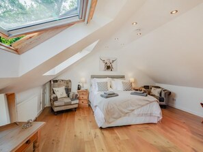 A bedroom with a sloped ceiling, a skylight, a bed with multiple pillows, a chair, bedside tables, and a wall-mounted artwork.