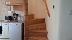 A wooden staircase leading to a landing with a kitchen area in the background. - 2 Bed in Ashford In The Water (oc-85823) (Ashford in the Water)