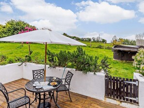 Eine Terrasse mit Tisch und Stühlen, einem weißen Sonnenschirm und Blick auf ein grünes Feld.