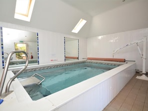 Uma piscina com uma escada de metal, uma luminária no teto e um espelho grande na parede.