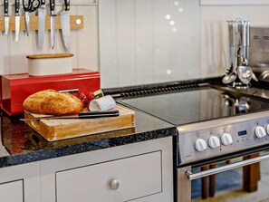 Cozinha com fogão de aço inoxidável, tábua com pão e queijo, e um eletrodoméstico vermelho ao fundo.