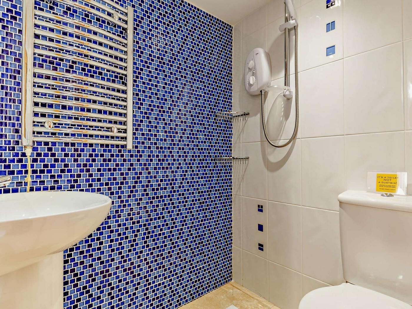 A bathroom with a blue mosaic wall, a white sink, a toilet, and a shower with a handheld showerhead.