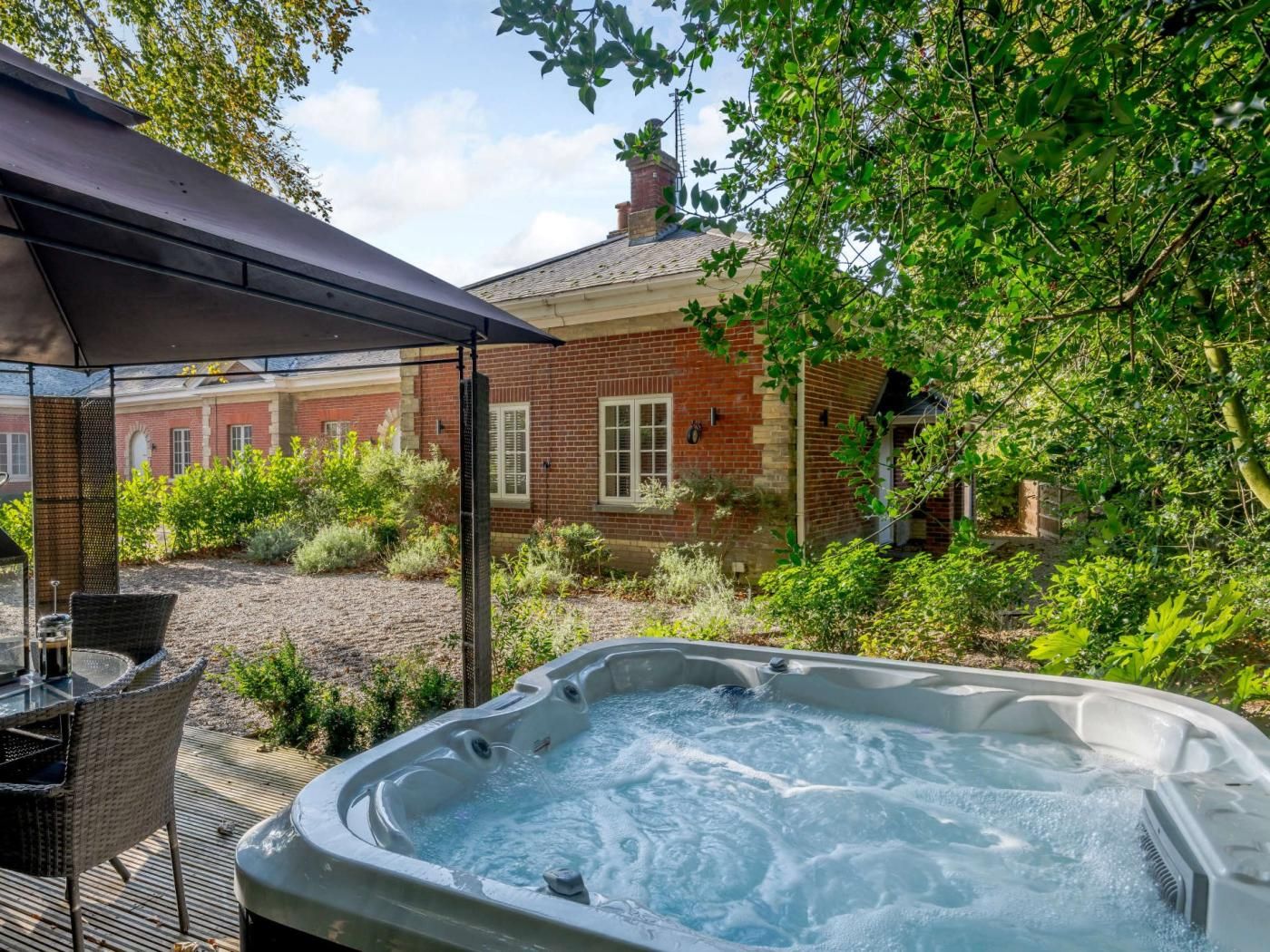 Boblebad med en terrasse, omgivet af grønt og en murstensbygning i baggrunden.