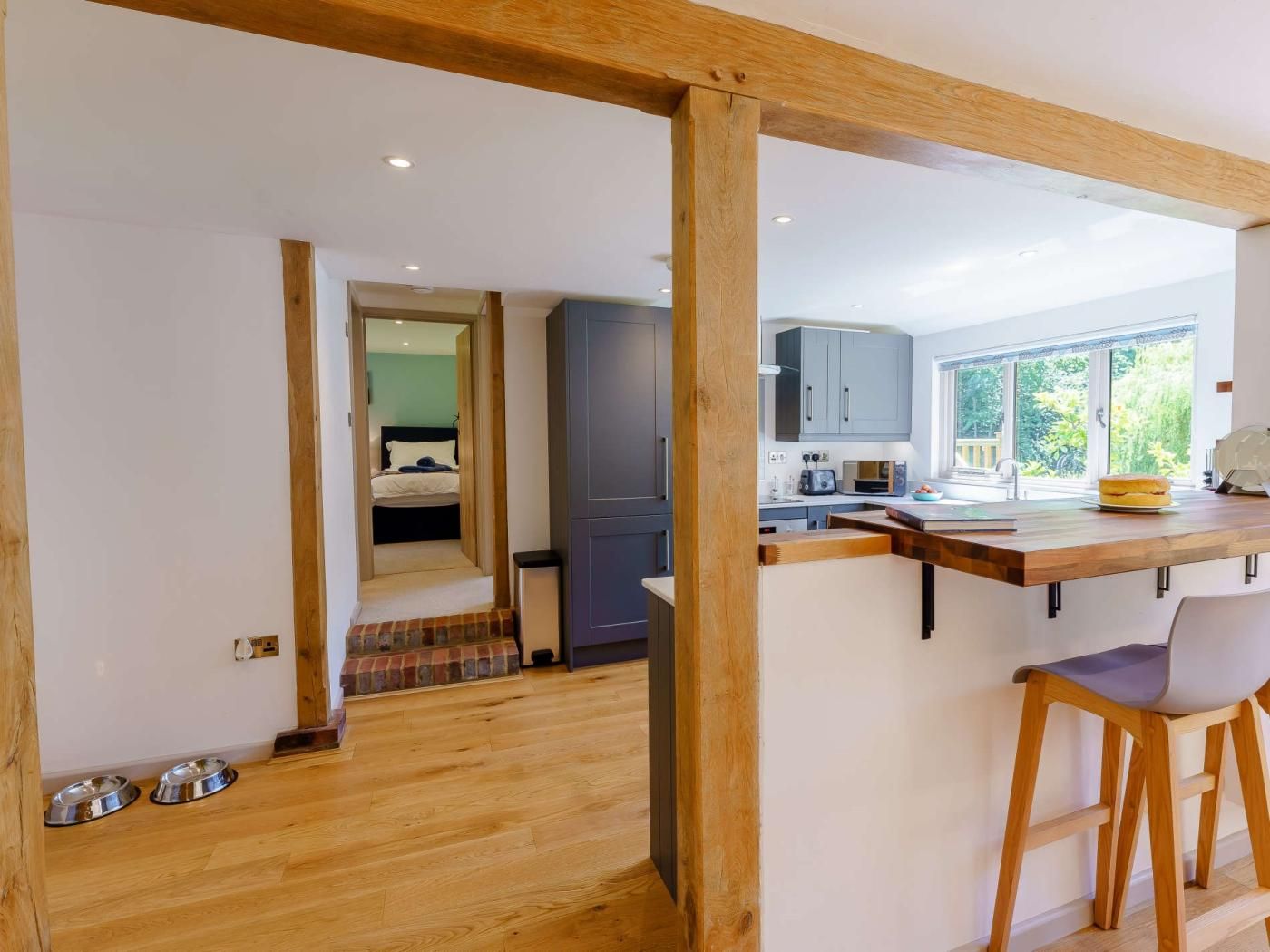 A modern kitchen with a wooden island, a dining area with a chair, and a view of the outdoors through large windows.