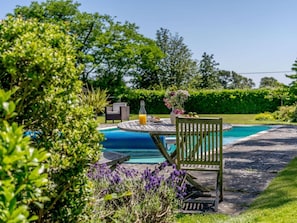 A poolside area with a wooden table, a bottle of orange juice, and a vase of flowers. - 2 Bed in Uckfield (oc-80504) (Framfield)