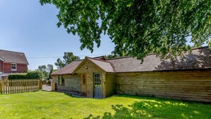 A wooden cabin with a front porch and a small attached shed, surrounded by a grassy yard and a wooden fence. - 2 Bed in Uckfield (oc-80504) (Framfield)