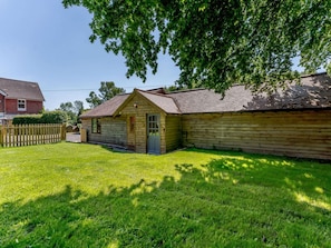 A wooden cabin with a front porch and a small attached shed, surrounded by a grassy yard and a wooden fence. - 2 Bed in Uckfield (oc-80504) (Framfield)