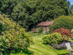 Una cabana de fusta envoltada per arbres densos i un jardí ben cuidat.
