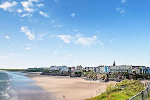 A coastal town with buildings along the beach, a clear sky, and a rocky shoreline. - 3 Bed in Tenby (oc-fb225) (Tenby)