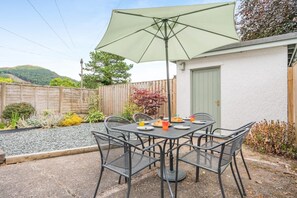 Eine Terrasse mit Tisch, Stühlen und Sonnenschirm, sowie eine Tür zu einem Haus.