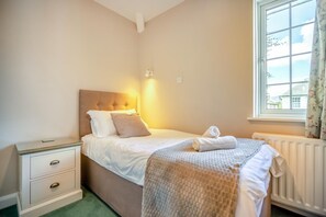 Un dormitorio con cama, mesitas de noche, una ventana con cortinas y un radiador.