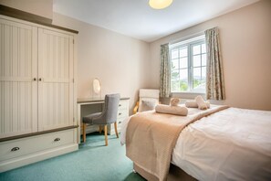 Ein Schlafzimmer mit großem Kleiderschrank, Schreibtisch mit Stuhl, Bett mit Daunendecke und einem Fenster mit Vorhängen.