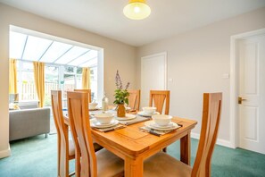 A dining area with a wooden table set for four, surrounded by chairs, with a window providing natural light. - 3 Bed in Keswick (oc-sz316) (Keswick)