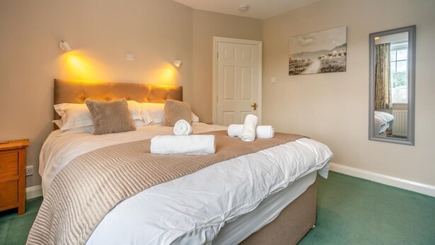 A neatly made bed with a headboard, two wall-mounted lamps, a door, a painting, and a mirror. - 3 Bed in Keswick (oc-sz316) (Keswick)