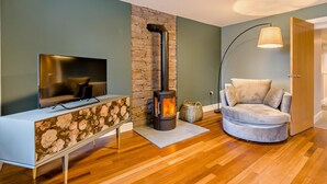 Una sala de estar con chimenea de piedra, un televisor sobre un mueble floral, un sofá redondo y una lámpara.