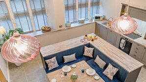 Una cocina moderna con comedor, que incluye una mesa de madera preparada para cuatro, una zona de estar empotrada con cojines y una lámpara colgante grande.
