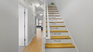 Una scala con gradini in legno e pareti bianche, che conduce a una stanza con una ventola a soffitto e vista su una finestra.