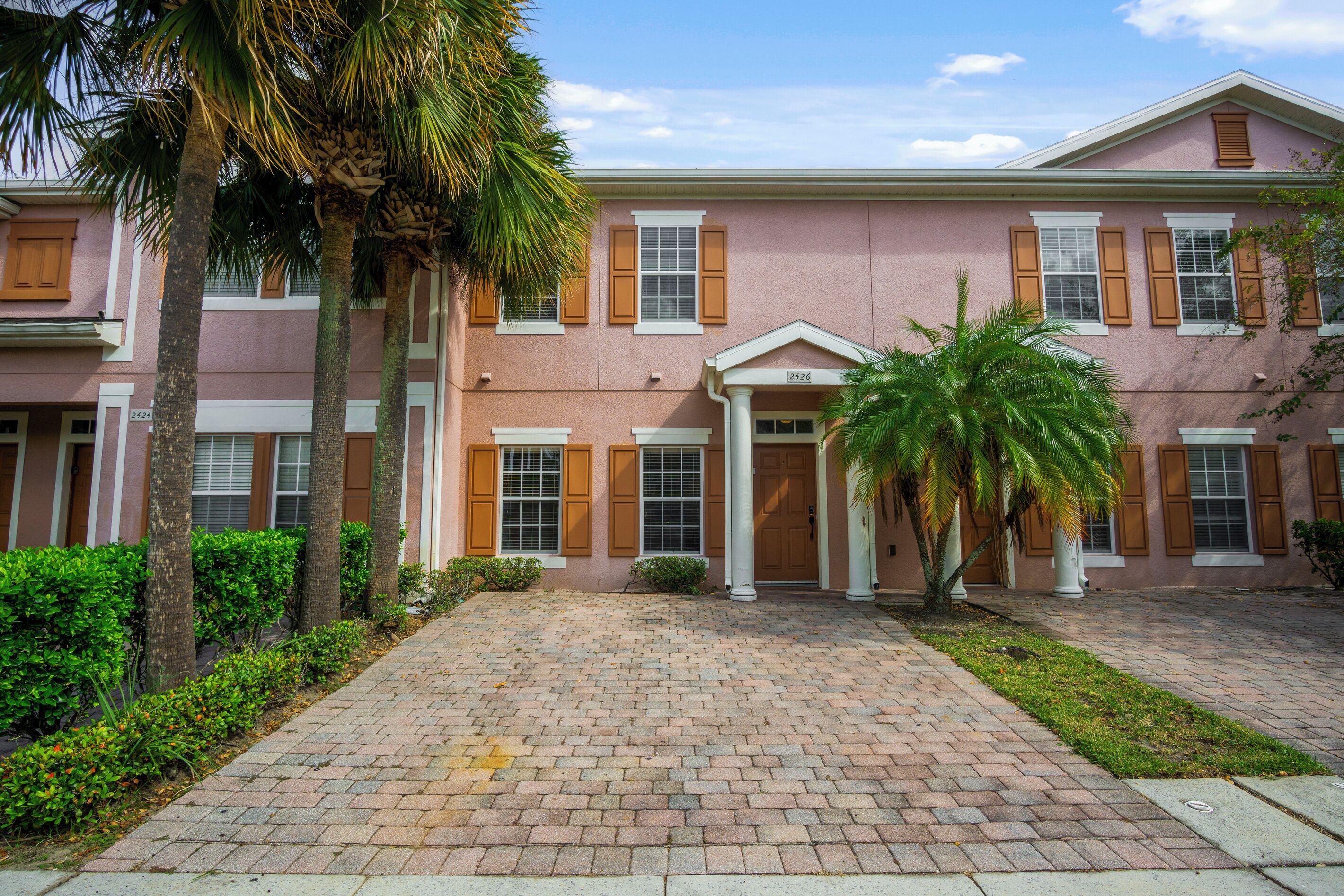 A pink building with a brick pathway, palm trees, and a clear sky.