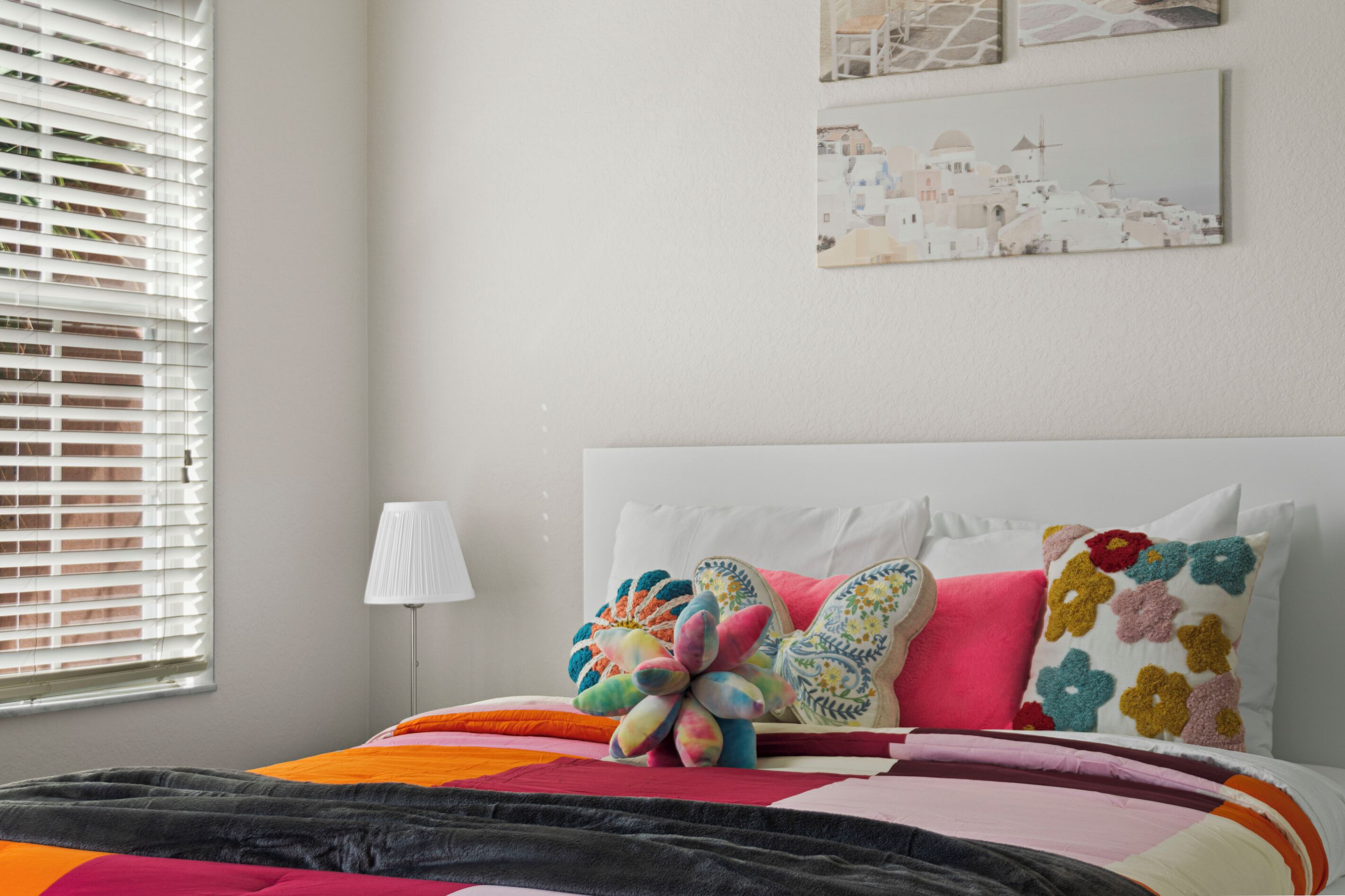 Un dormitorio con una cama, almohadas coloridas, una lámpara y obras de arte en la pared.