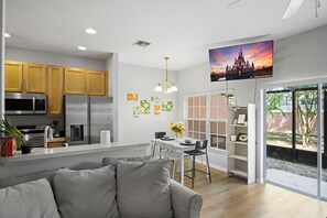 A modern kitchen with stainless steel appliances, a dining area with a white table and chairs, and a large flat-screen TV mounted on the wall. - Coral Cay 4BR Vacation Home,Close to Disney (Kissimmee)