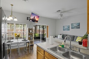 A modern kitchen with a dining area, a ceiling fan, and a TV mounted on the wall. - Coral Cay 4BR Vacation Home,Close to Disney (Kissimmee)