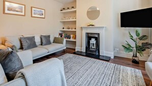 A living room with a sofa, fireplace, bookshelves, and a television. - 3 Bed in Brockenhurst (oc-nfl92) (Brockenhurst)