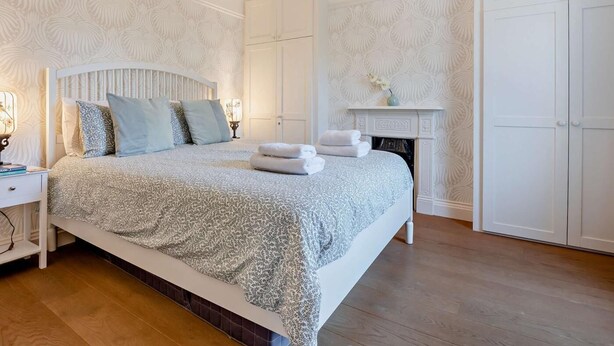 A bedroom with a large bed, a chandelier, a fireplace, and a wardrobe. - 3 Bed in Brockenhurst (oc-nfl92) (Brockenhurst)