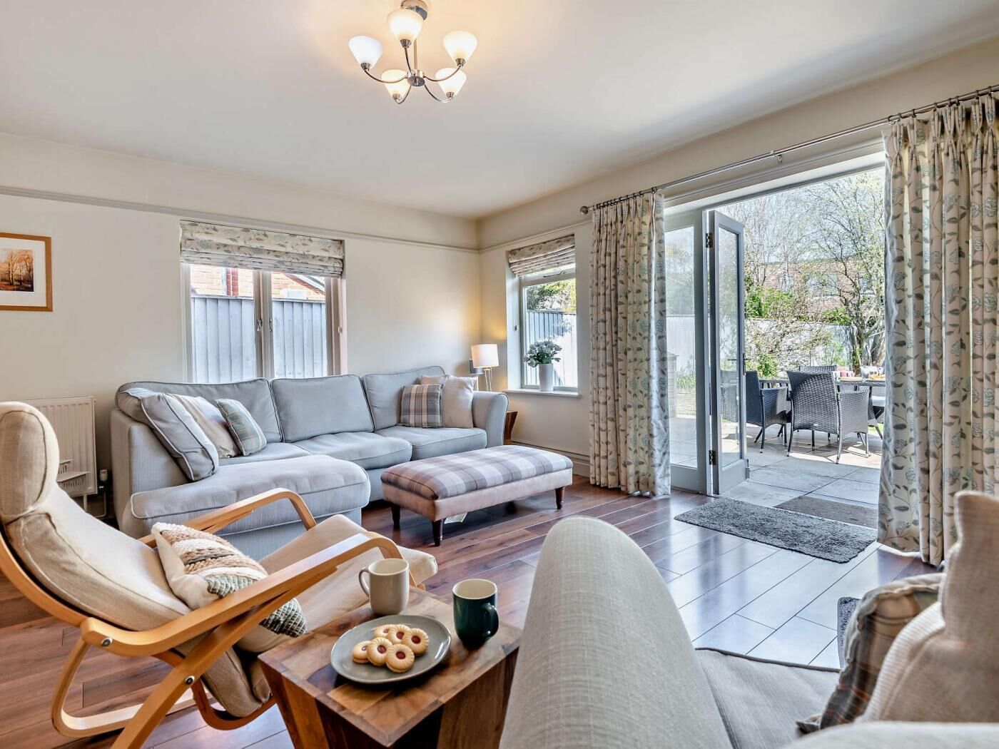 A modern living room with a sectional sofa, a wooden coffee table with cookies, a chair, and a view of the outdoors through a glass door.