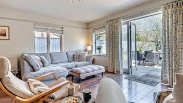 A modern living room with a sectional sofa, a wooden coffee table with cookies, a chair, and a view of the outdoors through a glass door.