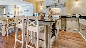 A modern kitchen with white cabinetry, a black countertop, and a dining area with white chairs. - 3 Bed in Brockenhurst (oc-nfl92) (Brockenhurst)