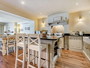 A modern kitchen with white cabinetry, a black countertop, and a dining area with white chairs. - 3 Bed in Brockenhurst (oc-nfl92) (Brockenhurst)