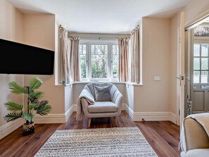 Ein Zimmer mit Fenster, Stuhl, Pflanze und Teppich.