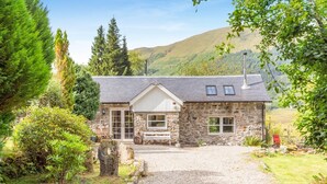 Ein Steinhaus mit Kiesauffahrt, einer Bank und Blick auf Hügel.