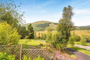 A rural landscape with a fenced area, a road, and a hill in the background. - 1 Bed in Callander (oc-pe173) (Strathyre)
