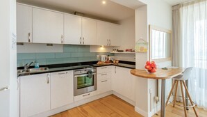 A modern kitchen with white cabinets, a black countertop, and a wooden dining table with a bowl of fruit.