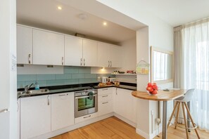 A modern kitchen with white cabinets, a black countertop, and a wooden dining table with a bowl of fruit.