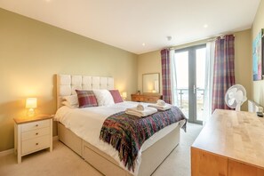 A hotel room with a bed, bedside table, nightstand, and a view of the outdoors.