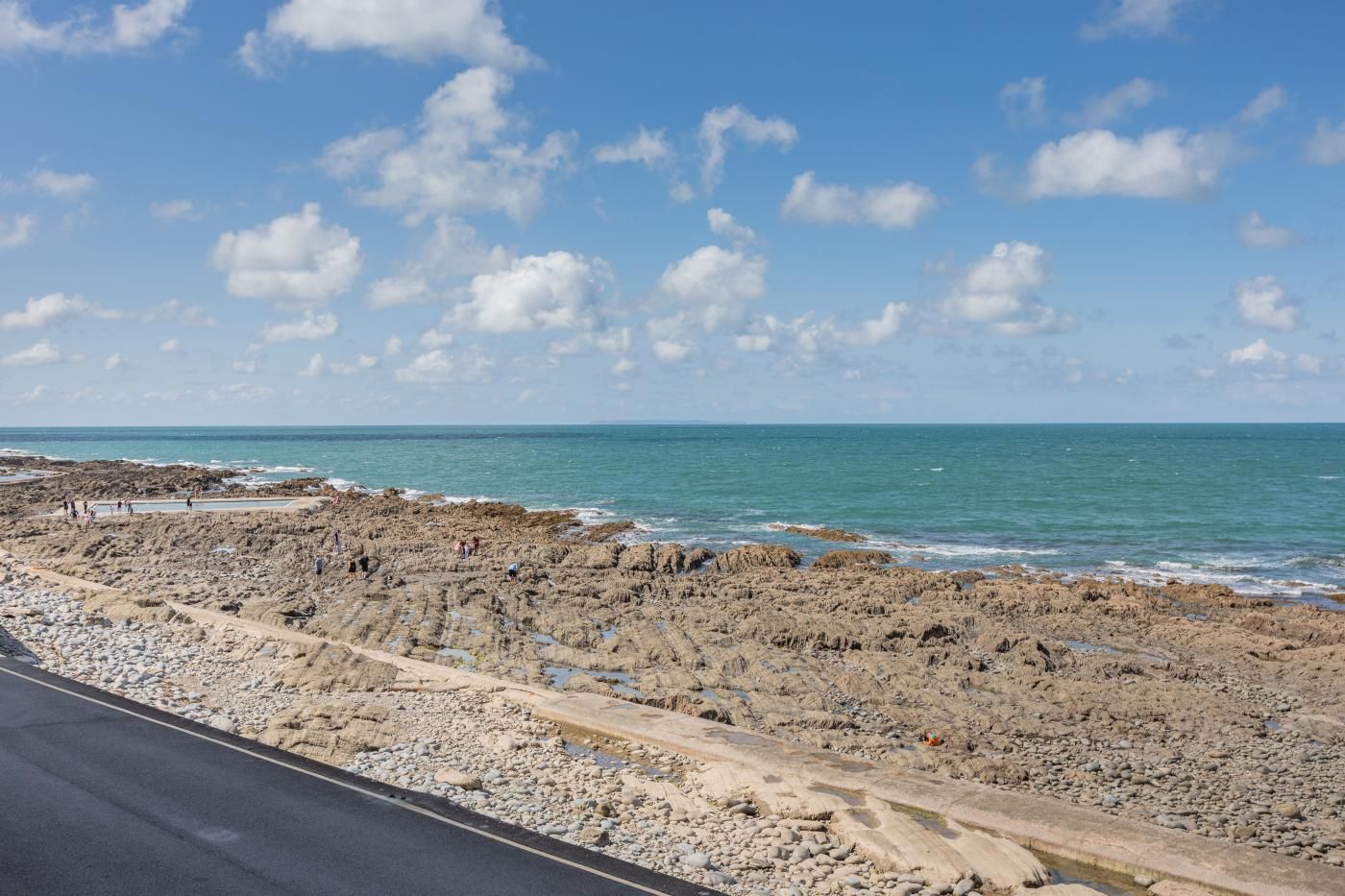 A rocky coastal road with a clear sky and calm sea.