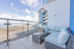 A balcony with a glass railing, a wicker sofa, and a table with breakfast items. - 3 Bed in Westward Ho! (oc-81483) (Westward Ho!)