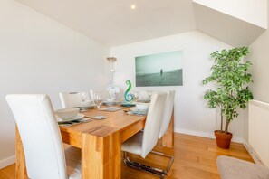 A dining area with a wooden table set for six, white chairs, a potted plant, and a framed picture on the wall. - 3 Bed in Westward Ho! (oc-81483) (Westward Ho!)