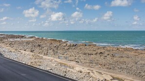 A rocky coastal road with a clear sky and calm sea.