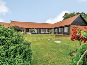 Un bâtiment à deux étages, doté d’un toit recouvert de tuiles rouges, d’un patio abrité et d’une pelouse bien entretenue.