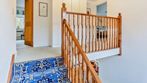 Eine Treppe mit Holzspindeln führt zu einer Zwischenebene, ein blaues gemustertes Teppich und eine weiße Wand mit einem gerahmten Bild.
