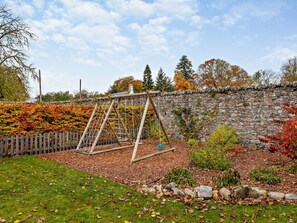 A wooden swing set in a garden with a stone wall and autumn foliage. - 3 Bed in Inverness (oc-ca134) (Farr House)